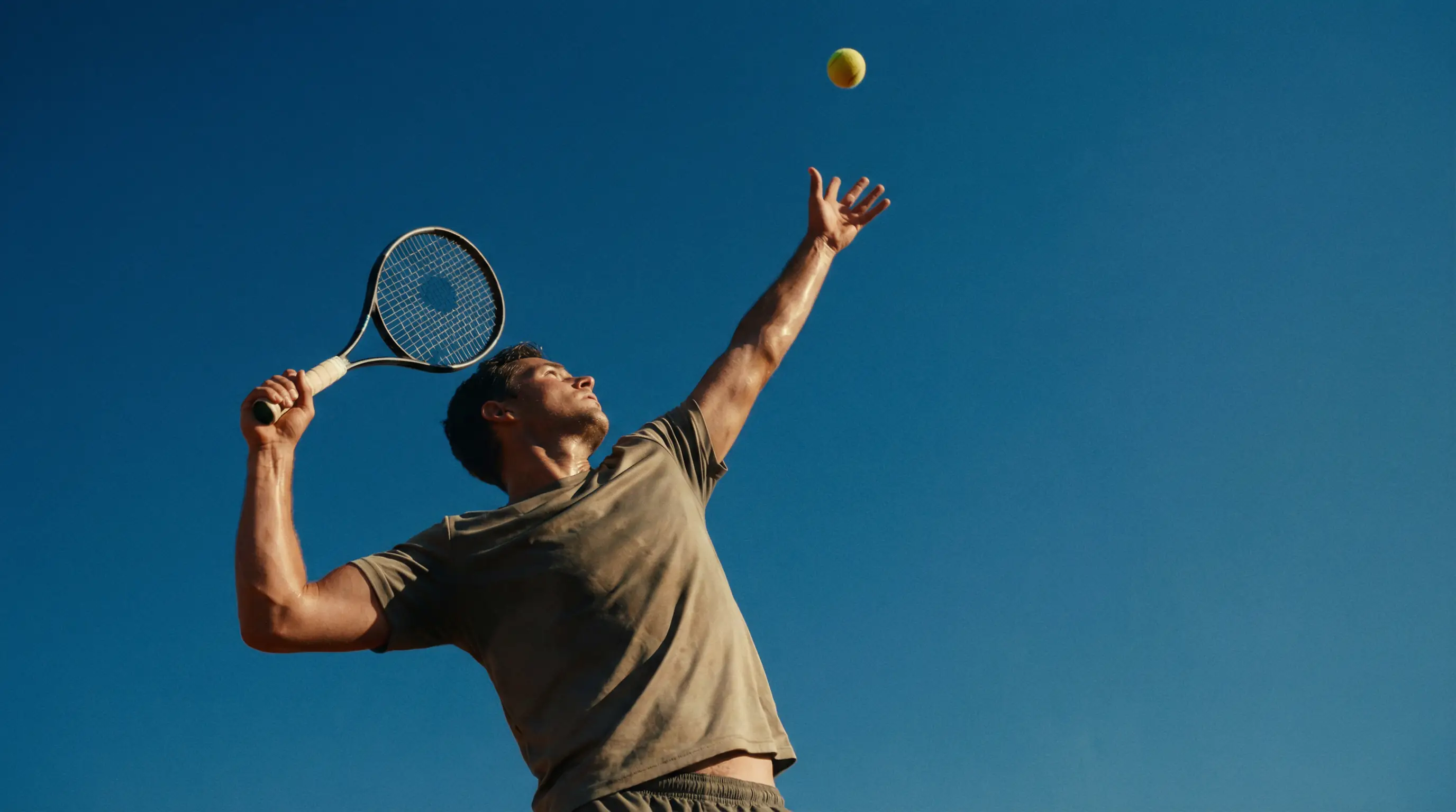 Joueur de tennis en plein lancer de balle au service vu en contre-plongée avec le ciel en fond